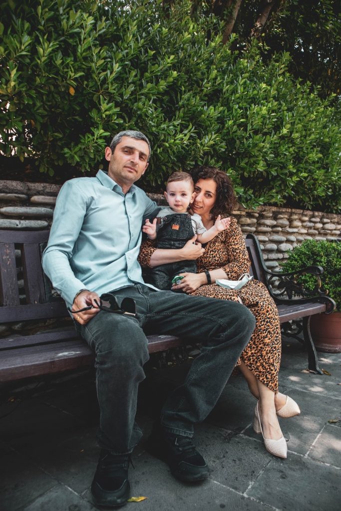Padre e madre seduti su una panchina con bambino piccolo in piedi tra loro
